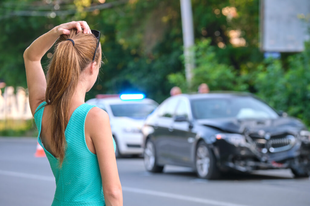 Stressed woman driver standing on street side shocked after car accident. Road safety and insurance concept.