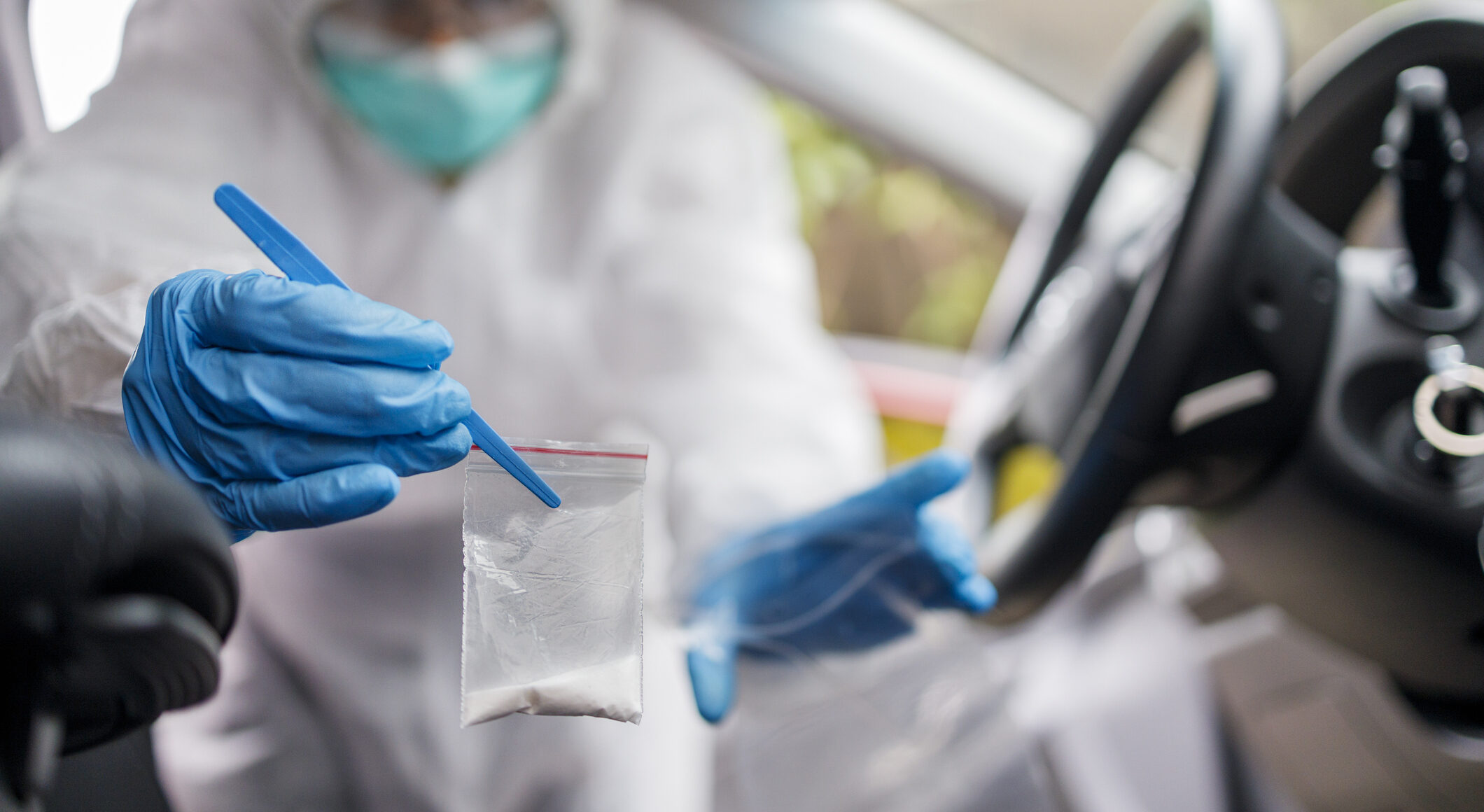 Police officer in protective suit finding narcotics in a car which is now a crime scene